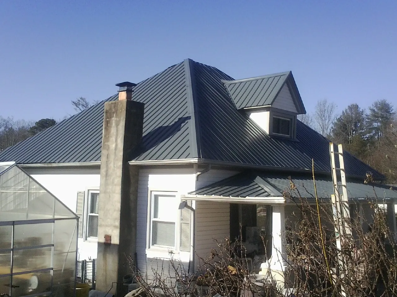 Dark blue standing seam metal roof on a white farmhouse with dormer — Slate & Tile Roof Repair by Roofing Brothers in Center