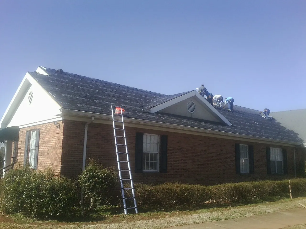 Crew tearing shingles off a brick ranch roof with a ladder set — Metal Roof Repair work by our crew in Center