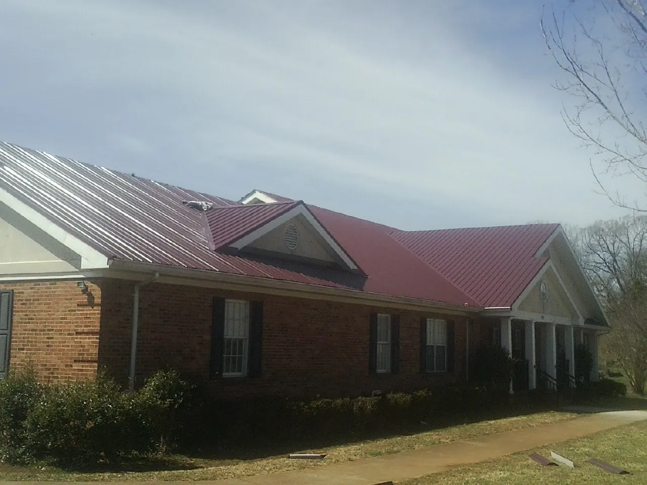 Red metal roof with gabled entries on a long brick building, from a Hail Damage Roof Repair job in Center
