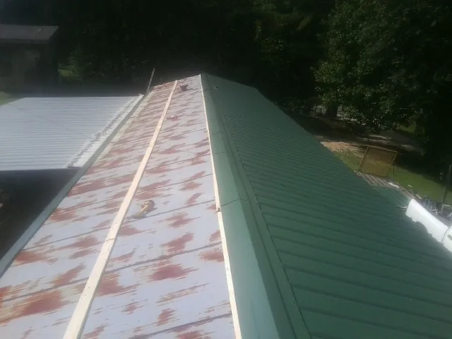 Old rusted panels beside newly installed green metal roofing — Wind Damage Roof Repair by Roofing Brothers in Center