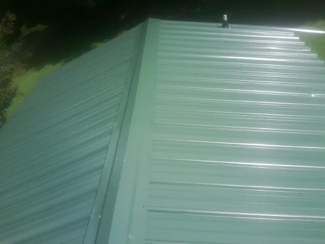 New green metal panels meeting at the ridge of a roof — Flat Roof Repair work by our crew in Center
