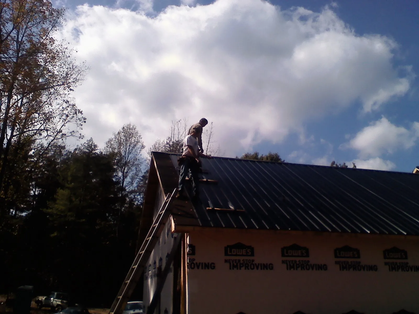 Roofer fastening dark metal panels high against a cloudy sky, from a Roof Inspection job in Center