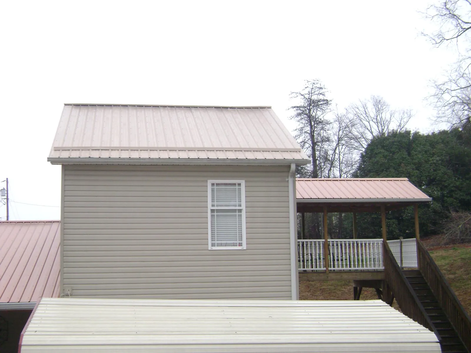 Tan metal roofs on a two story addition and attached porch, from a Roof Replacement job in Center