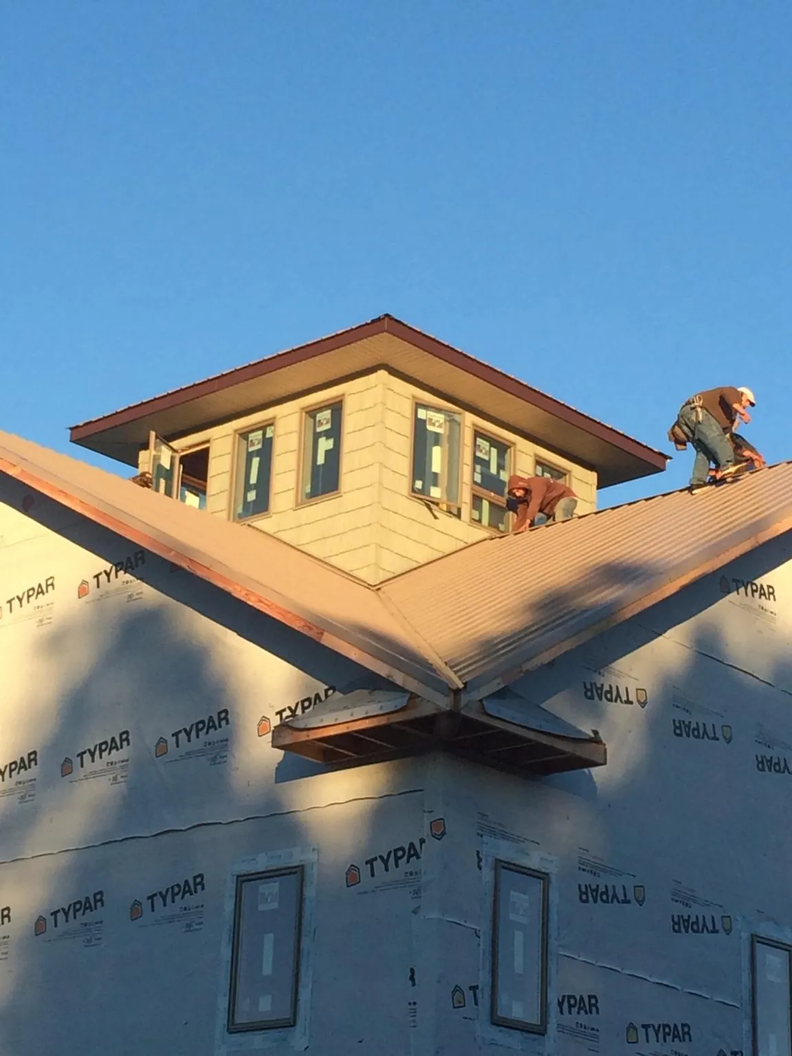 Roofers working around a rooftop cupola on a new metal roof at sunset — Roof Waterproofing in Center by Roofing Brothers